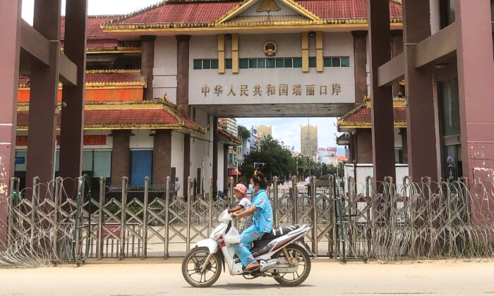 A woman and child ride a scooter past the China-Myanmar border gate in Muse, Burma on July 5, 2021. (STR/AFP via Getty Images)