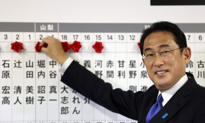 Japan's Prime Minister and ruling Liberal Democratic Party leader Fumio Kishida puts rosettes by successful general election candidates' names on a board at the party headquarters in Tokyo on Oct. 31, 2021. (Behrouz Mehri, Pool via AP)