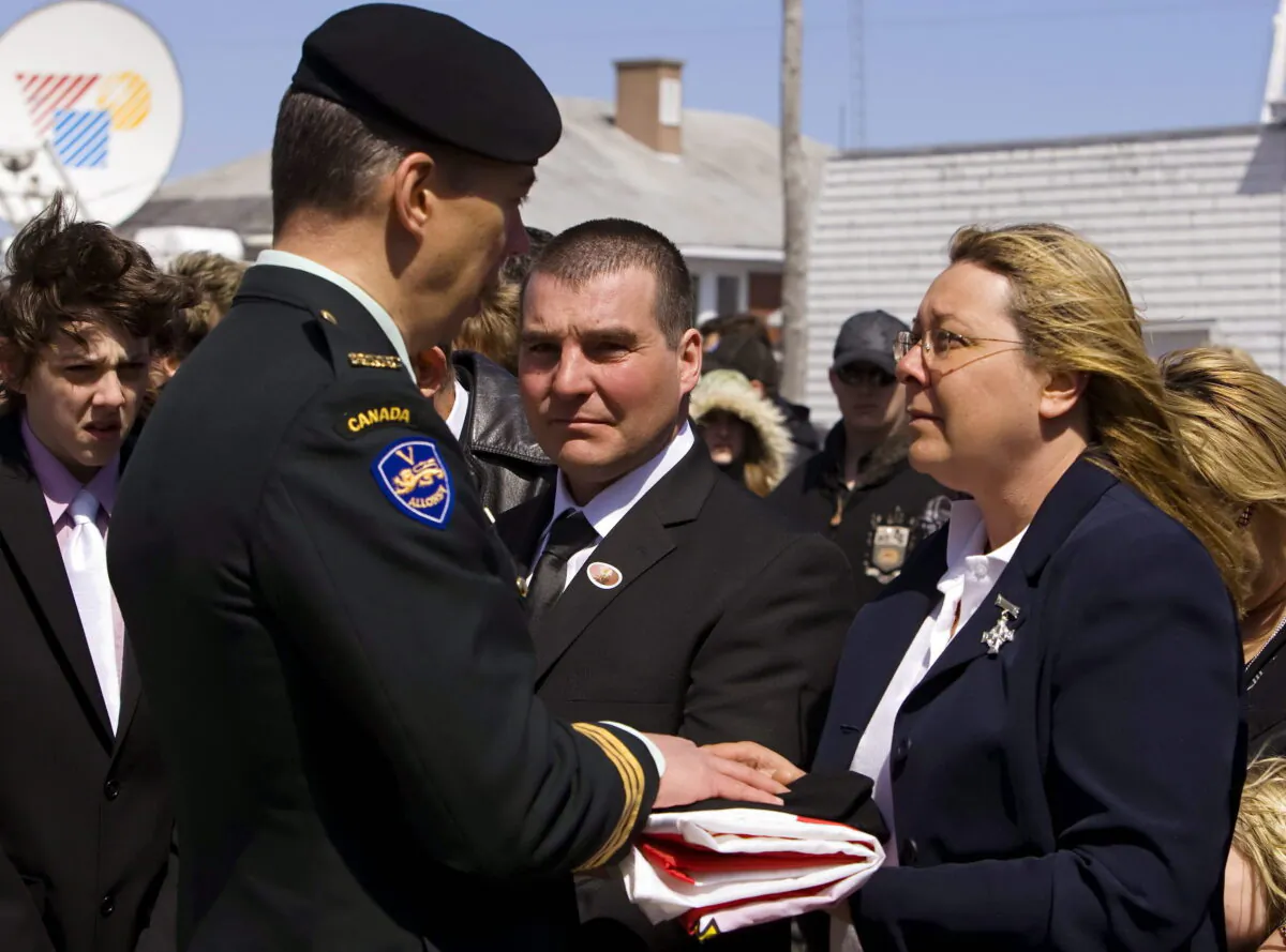 Josee Simard, right, mother of Canadian Trooper Karine Blais, receives the Canadian Forces Ensign from Lt.-Col. Stephane Tremblay after a funeral service as Marco Sergerie, (C), looks on in Les Méchins, Que on April 24, 2009. (The Canadian Press/Clement Allard)