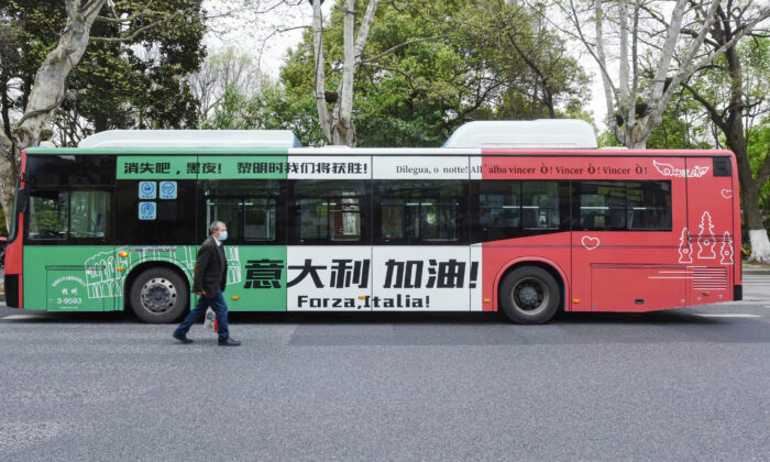 A man walks past a bus with a message supporting Italy in their efforts against the COVID-19 coronavirus in Hangzhou in China's eastern Zhejiang Province on March 24, 2020. (STR/AFP via Getty Images)