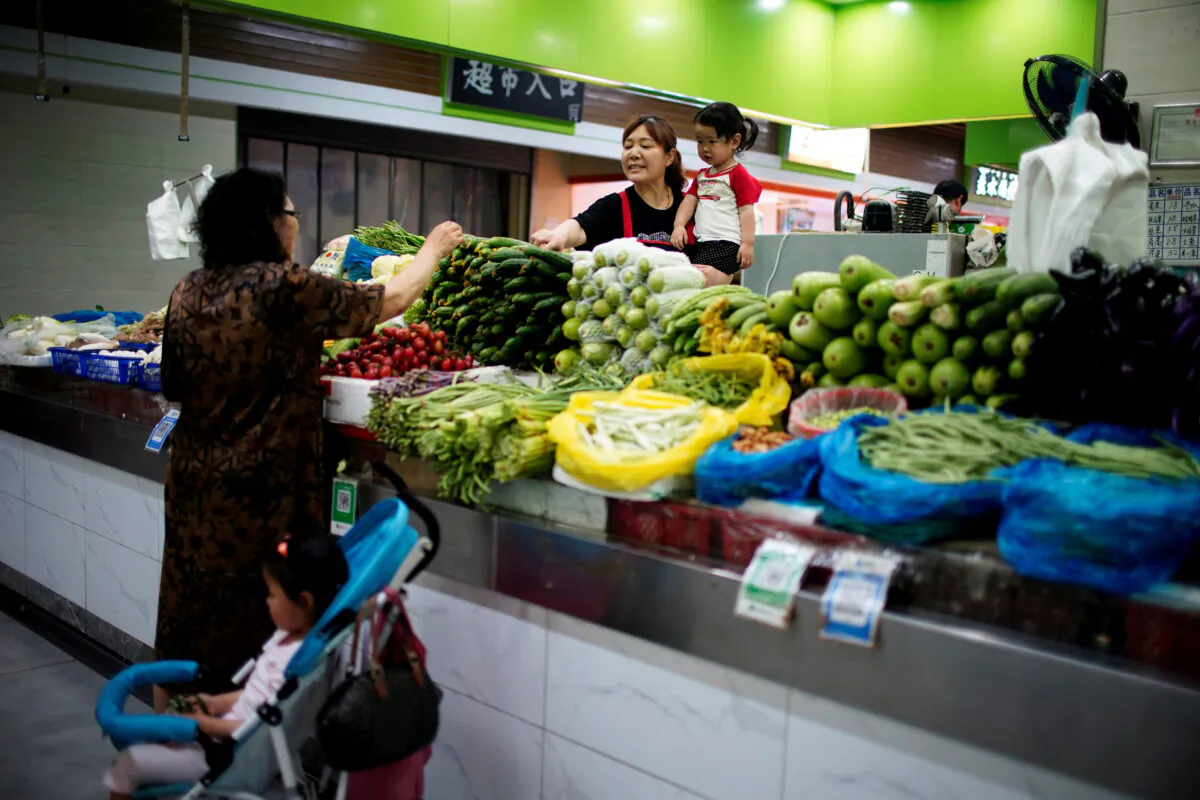 Two grandmothers with their granddaughter trade vegetables at a market on the outskirts of Shanghai, China, on June 3, 2021. (Aly Song/File Photo/Reuters)