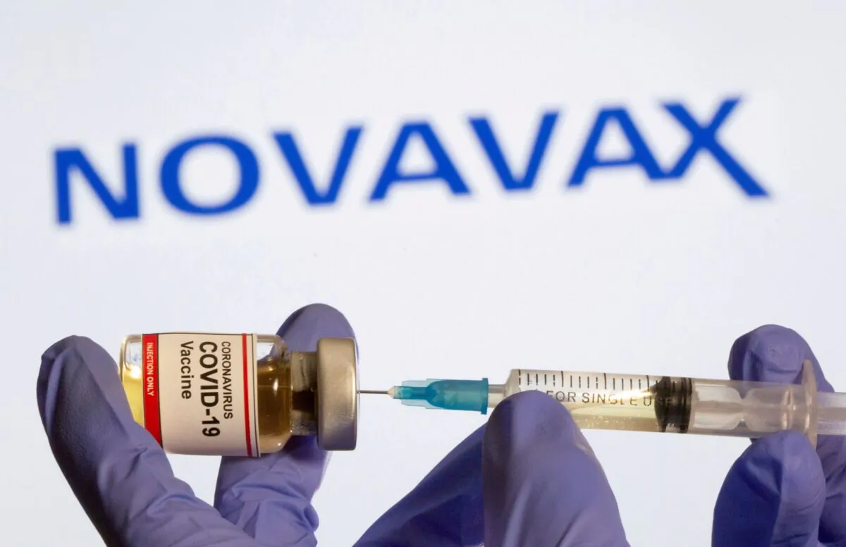 A woman holds a small bottle labeled with a "Coronavirus COVID-19 Vaccine" sticker and a medical syringe in front of displayed Novavax logo in this illustration taken on Oct. 30, 2020. (Dado Ruvic/Reuters)