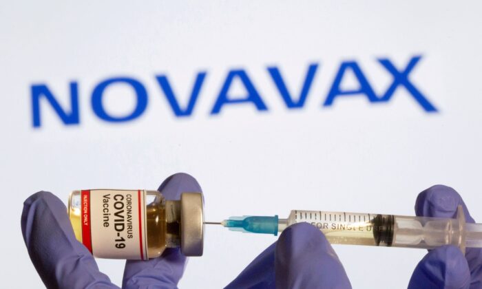 A woman holds a small bottle labeled with a "Coronavirus COVID-19 Vaccine" sticker and a medical syringe in front of the displayed Novavax logo in this illustration taken on Oct. 30, 2020. (Dado Ruvic/Reuters)