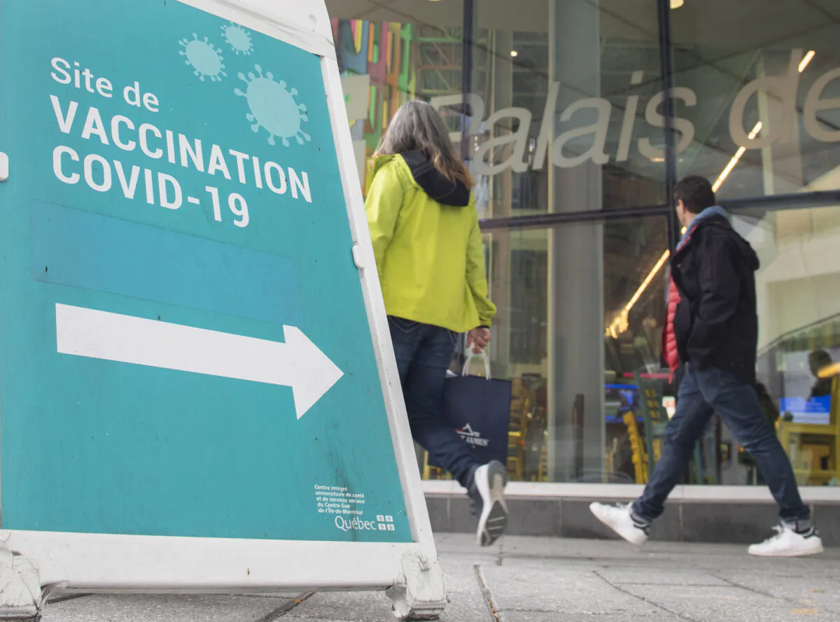 People walk by a sign advertising a COVID-19 vaccination site, in Montreal, Oct. 3, 2021. (The Canadian Press/Graham Hughes)