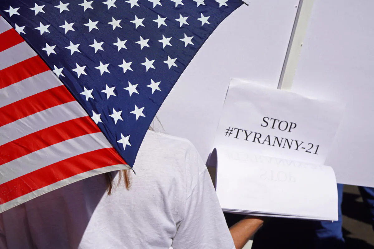 This protester, holding a flag umbrella and a sign, was among 200 people gathered at a Worldwide Walkout rally against COVID-19 vaccines and mandates in Phoenix on Nov. 3, 2021. (Allan Stein/Epoch Times)