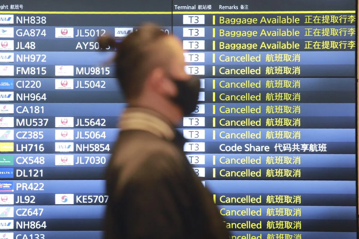 A man wearing a face mask walks by a flight information board at the Haneda International Airport in Tokyo, Japan, on Dec. 28, 2020. (Koji Sasahara/AP Photo)
