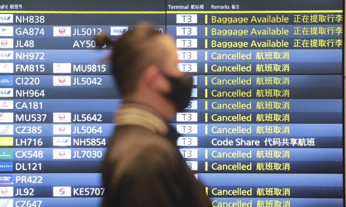 A man wearing a face mask walks by a flight information board at the Haneda International Airport in Tokyo, Japan, on Dec. 28, 2020. (Koji Sasahara/AP Photo)