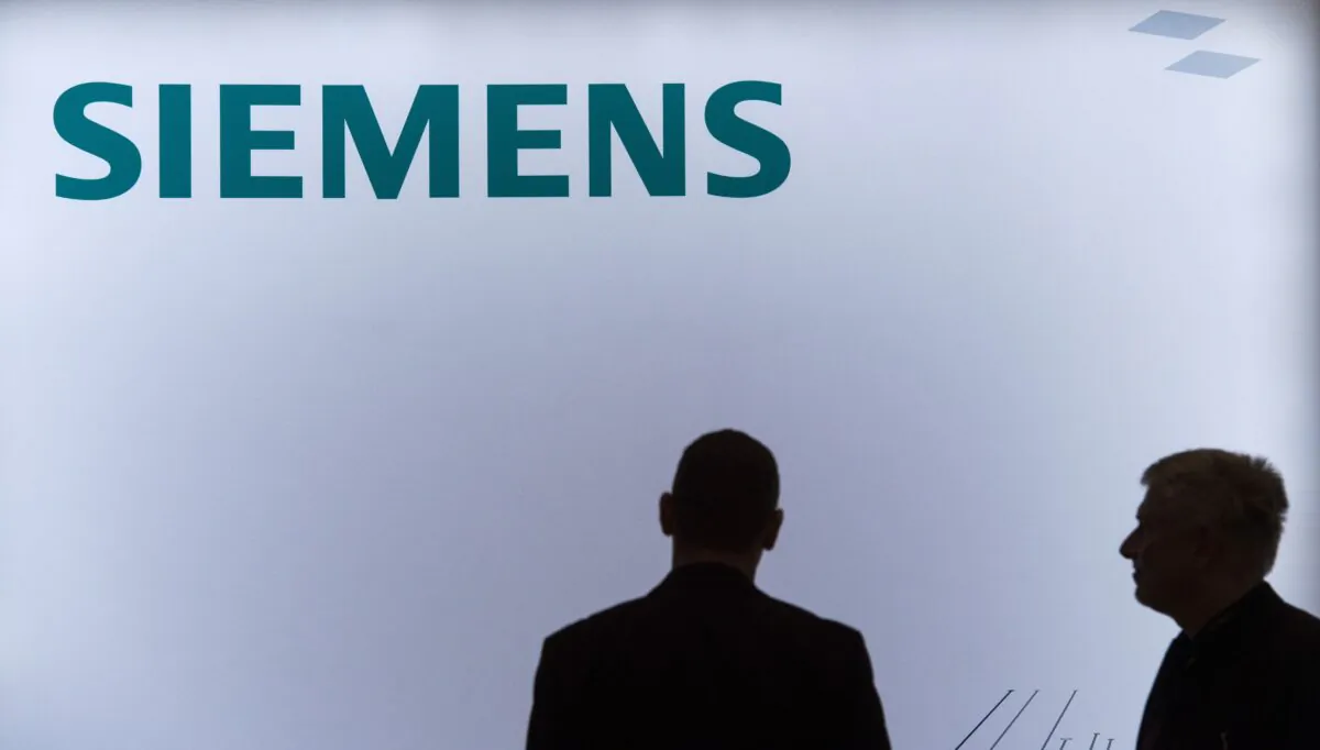 Employees of German industrial giant Siemens stand in front of a company logo during a press conference in Berlin on Nov. 12, 2015. (John Macdougall/AFP via Getty Images)