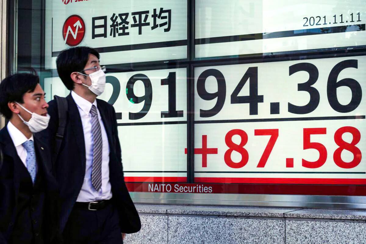 Men wearing protective masks walk in front of an electronic stock board showing Japan's Nikkei 225 index at a securities firm in Tokyo, Japan on Nov. 11, 2021. (Eugene Hoshiko/AP Photo)