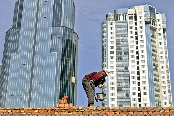 A construction worker lays bricks near high-rise buildings in Shanghai, China, on March 31, 2005.  (AFP PHOTO/LIU Jin)
