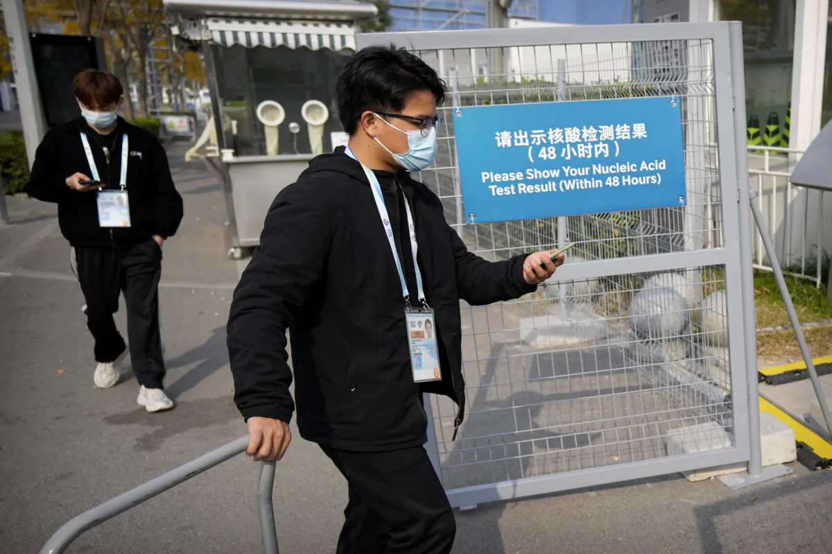 Workers wearing face masks to protect against COVID-19 walk past a sign reminding visitors to show proof of a negative coronavirus test to enter the Beijing National Aquatics Center during the World Wheelchair Curling Championship, a test event for the 2022 Winter Olympics, in Beijing, on Oct. 29, 2021. (Mark Schiefelbein/AP Photo)