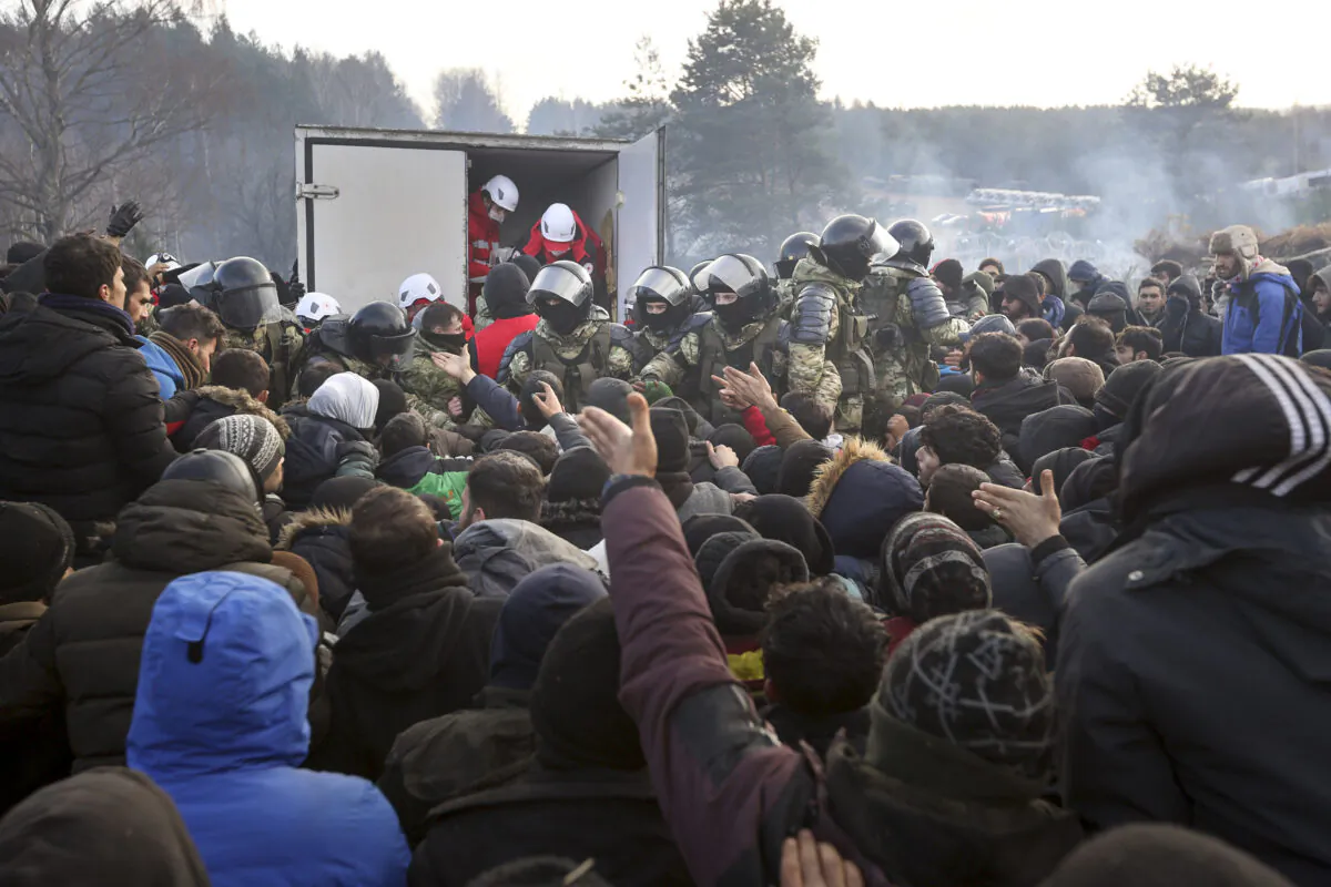Belarusian servicemen control the situation while migrants get humanitarian aid as they gather at the Belarus-Poland border near Grodno, Belarus on Nov. 12, 2021. (Ramil Nasibulin/BelTA pool photo via AP)