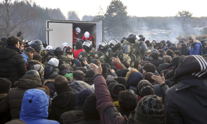 Belarusian servicemen control the situation while migrants get humanitarian aid as they gather at the Belarus-Poland border near Grodno, Belarus on Nov. 12, 2021. (Ramil Nasibulin/BelTA pool photo via AP)