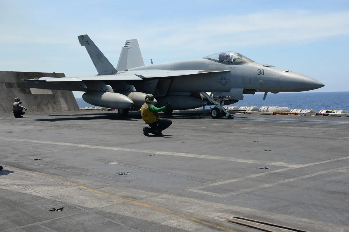 A sailor signals an FA-18 hornet fighter jet to take off from U.S. aircraft carrier Theodore Roosevelt in the South China Sea on April 10, 2018. (Ted Aljibe/AFP via Getty Images)