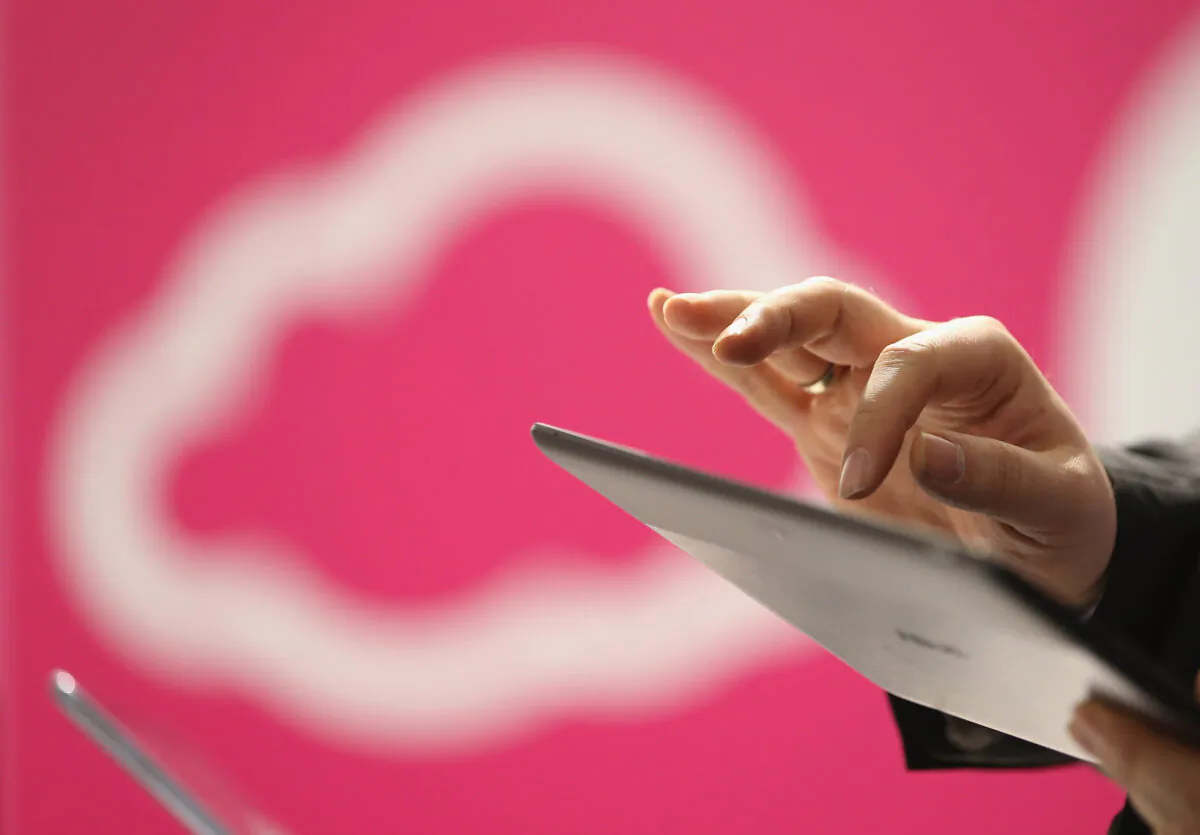 A visitor tries out a tablet computer next to a cloud computing and technology symbol at the Deutsche Telekom stand at the 2013 CeBIT technology trade fair in Hanover, Germany, on March 5, 2013. (Sean Gallup/Getty Images)