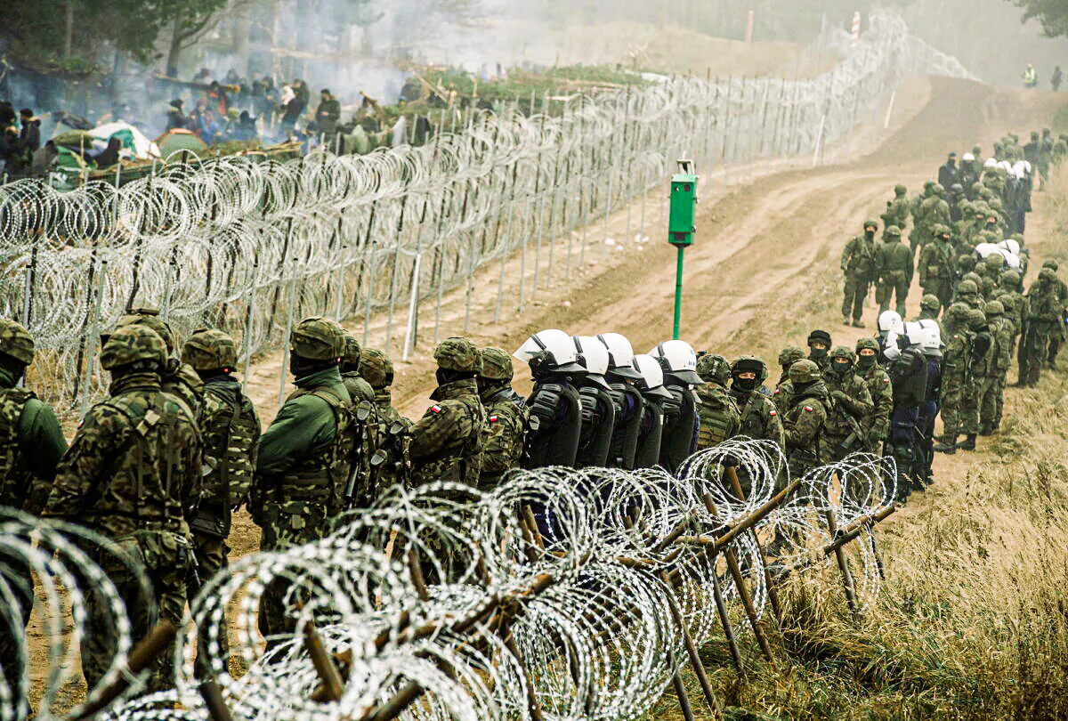 Polish soldiers and police watch migrants at the Poland-Belarus border near Kuznica, Poland, in this photograph released by the Territorial Defence Forces on Nov. 12, 2021. (Irek Dorozanski/DWOT/Handout via Reuters)