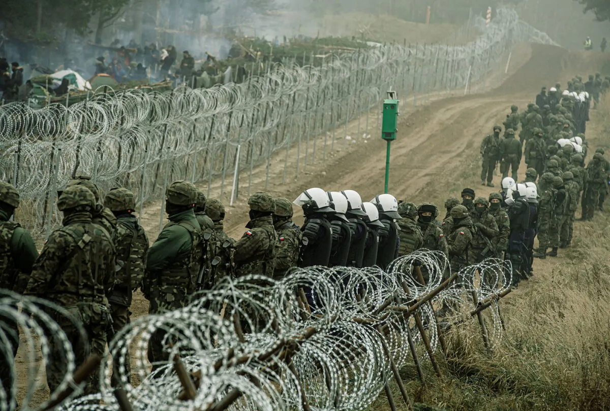 Polish soldiers and police watch illegal immigrants at the Poland/Belarus border near Kuznica, Poland, in this photograph released by the Territorial Defence Forces, on Nov. 12, 2021. (Irek Dorozanski/DWOT/via Reuters)