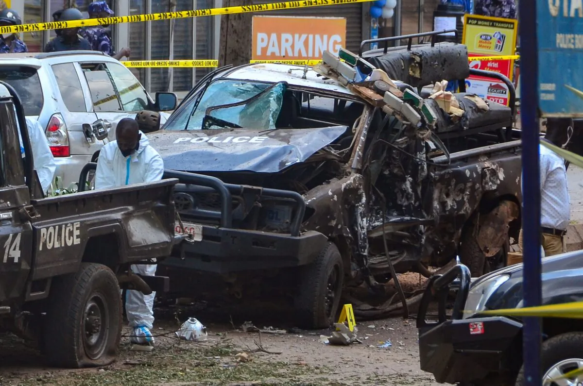 Police officers in personal protective equipment (PPE) investigate around the police cars destroyed by a bomb explosion in front of Central Police Station in Kampala, Uganda, on Nov. 16, 2021. (Lawrence Kitatta/AFP via Getty Images)