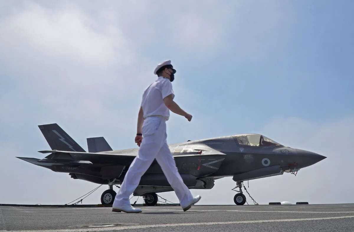 A seaman walks past an F-35B Lightning multirole combat aircraft along the deck of the HMS Queen Elizabeth aircraft carrier while moored in the new port of Cyprus's southern city of Limassol on July 1, 2021. (Roy Issa/AFP via Getty Images)