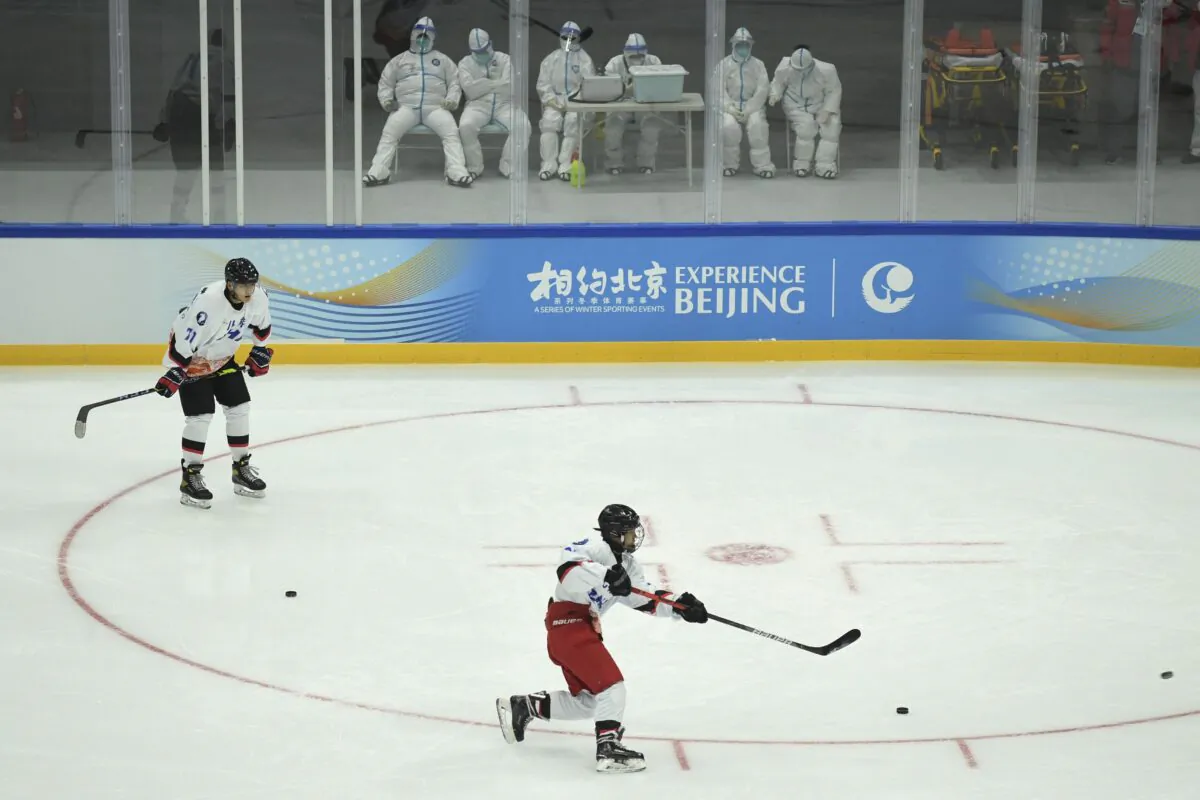Athletes take part in an ice hockey training session as health workers (top) stand by during a 2022 Beijing Winter Olympic Games test event, at the National Indoor Stadium in Beijing on Nov. 11, 2021. (Wang Zhao/AFP via Getty Images)