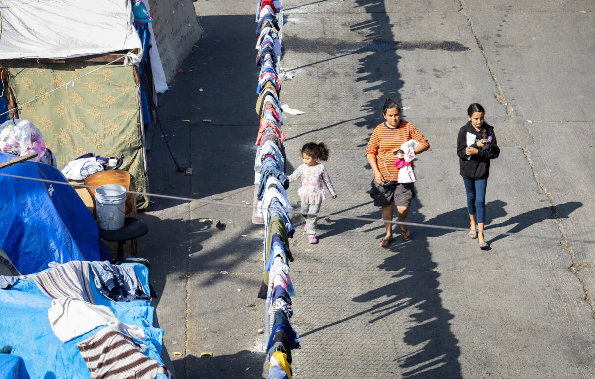A migrant family walks along a fenced encampment guarded by Mexican Police in Tijuana, Mexico, on Nov. 6, 2021. (John Fredricks/The Epoch Times)