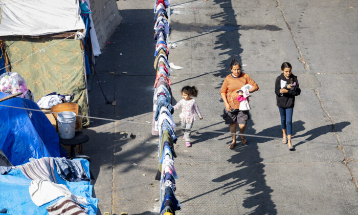 A migrant family walks along a fenced encampment guarded by Mexican Police in Tijuana, Mexico, on Nov. 6, 2021. (John Fredricks/  Pezou)