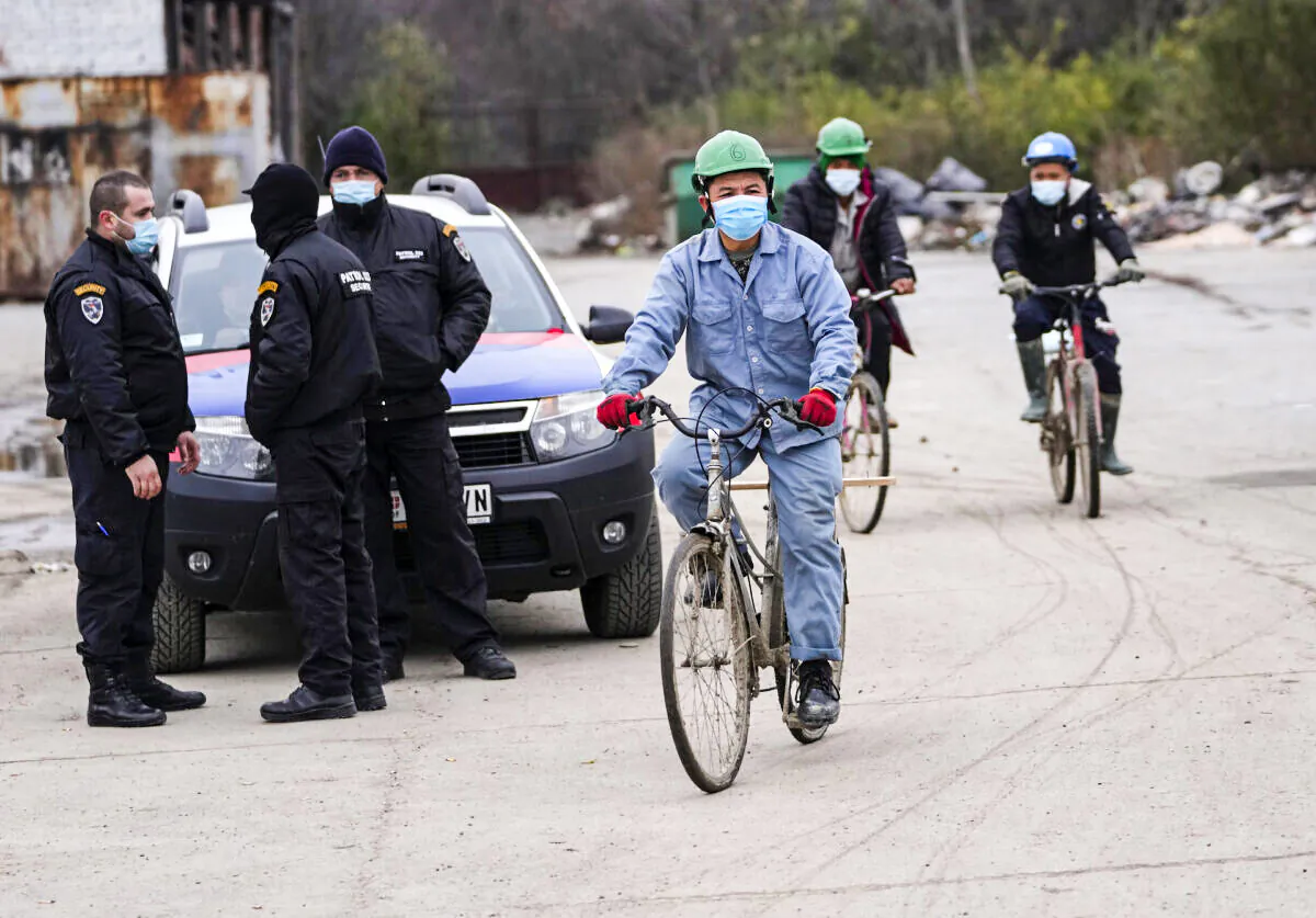 Vietnamese workers who are helping construct the first Chinese car tire factory in Europe ride bicycles past security officers near the northern Serbian town of Zrenjanin, 50 kilometers north of Belgrade, Serbia, Nov. 18, 2021. (Darko Vojinovic/AP Photo)