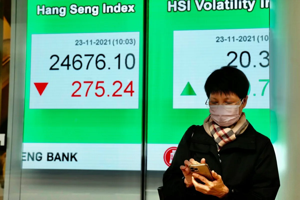 A woman wearing a face mask uses her smartphone a bank's electronic board showing the Hong Kong share index in Hong Kong on Nov. 23, 2021. (Kin Cheung/AP Photo)