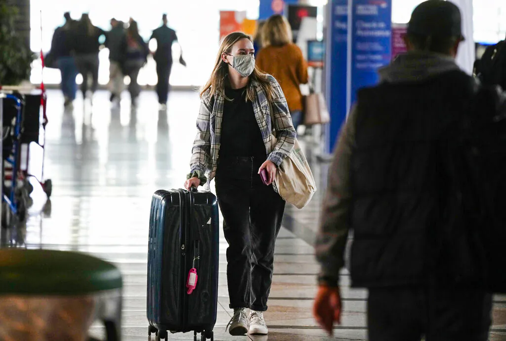 A traveler wears a face covering while heading to the American Airlines check-in counter at Denver International Airport in Denver, Colo., as the Thanksgiving Day holiday approaches Nov. 23, 2021. (AP Photo/David Zalubowski)