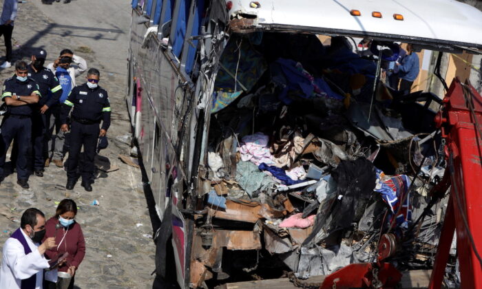 A priest blesses the bus at the scene where at least 19 people were killed and 20 more injured after a passenger bus traveling on a highway crashed into a house, according to authorities, in San Jose El Guarda, Mexico, Nov. 26, 2021.(Luis Cortes/Reuters)