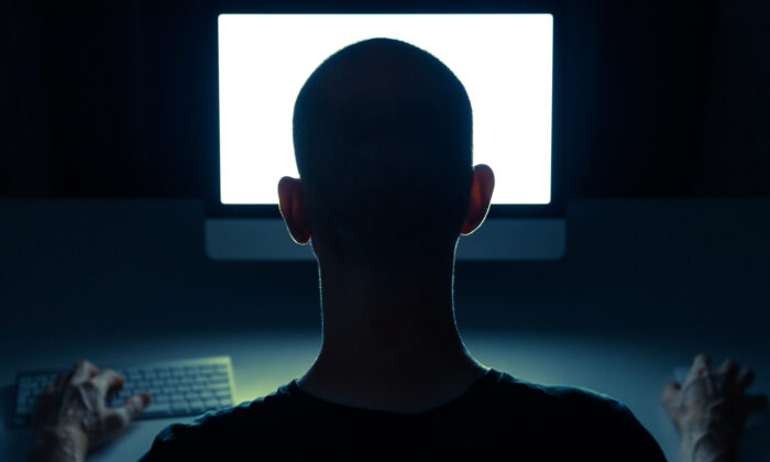 Man browsing the internet on a computer in a dark room. (sanderstock/Adobe Stock)