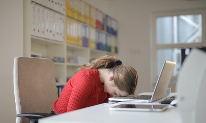 A woman with her head down at a desk.(pexels)