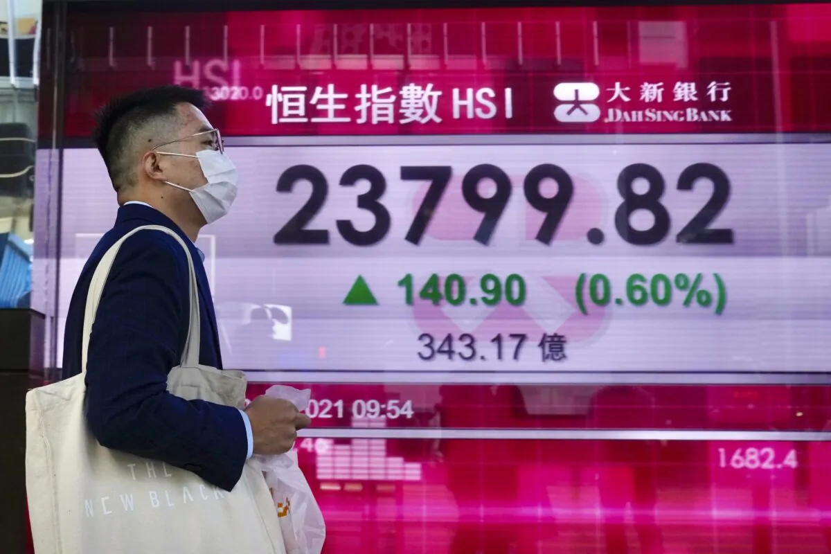 A man wearing a face mask walks past a bank's electronic board showing the Hong Kong share index in Hong Kong, on Dec. 2, 2021. (Kin Cheung/AP Photo)