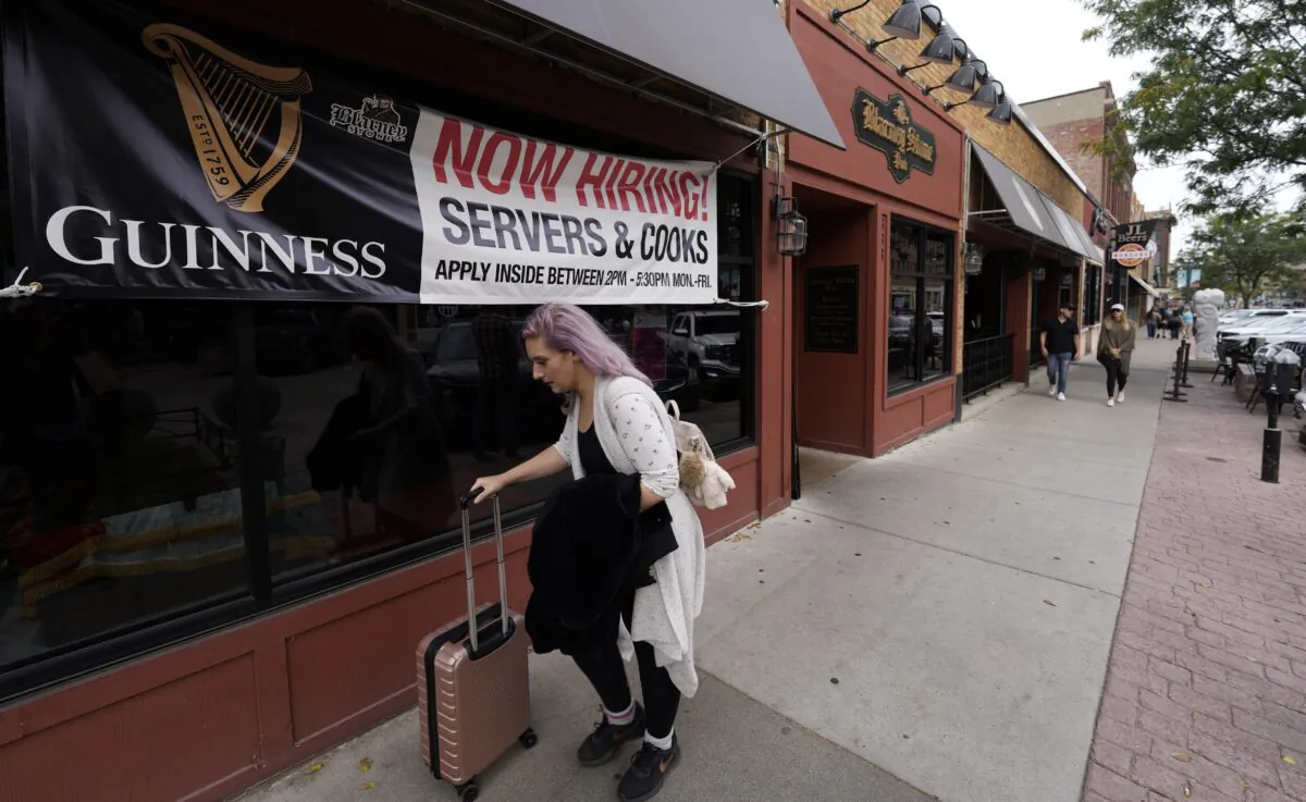 A traveller wheels her baggage past a now hiring sign outside a bar and restaurant, in Sioux Falls, S.D., on Oct. 9, 2021. (David Zalubowski/AP Photo)