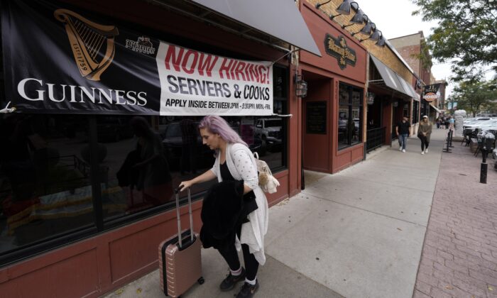 A traveller wheels her baggage past a now hiring sign outside a bar and restaurant, in Sioux Falls, S.D., on Oct. 9, 2021. (David Zalubowski/AP Photo)