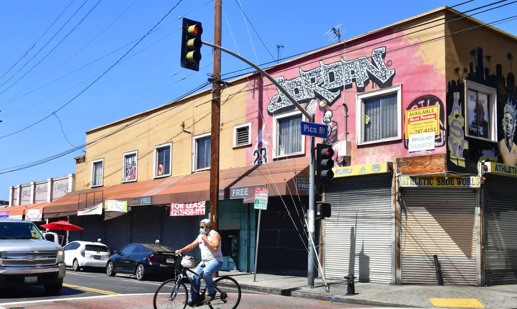 A man adjusts his face mask riding past closed shopfronts in Los Angeles on May 4, 2020. (Frederic J. Brown/AFP via Getty Images)