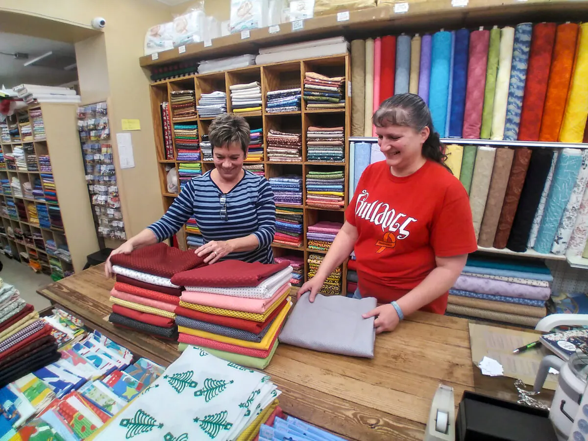 Georgia Wertz-Woolery (L), owner of Wertz Variety Store, folds fabric with employee Anna Pratt at the store in West Milton, Ohio, on Dec. 7, 2021. (Michael Sakal/The Epoch Times)