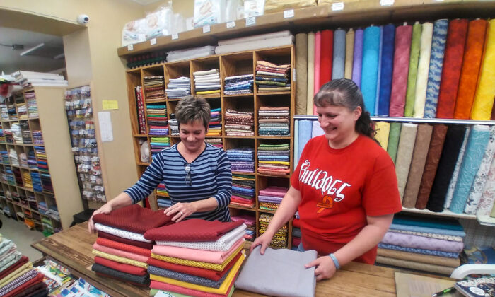 Georgia Wertz-Woolery (L), owner of Wertz Variety Store, folds fabric with employee Anna Pratt at the store in West Milton, Ohio, on Dec. 7, 2021. Supply chain issues have made it difficult for Wertz-Woolery to keep some items in stock. (Michael Sakal/The Epoch Times)