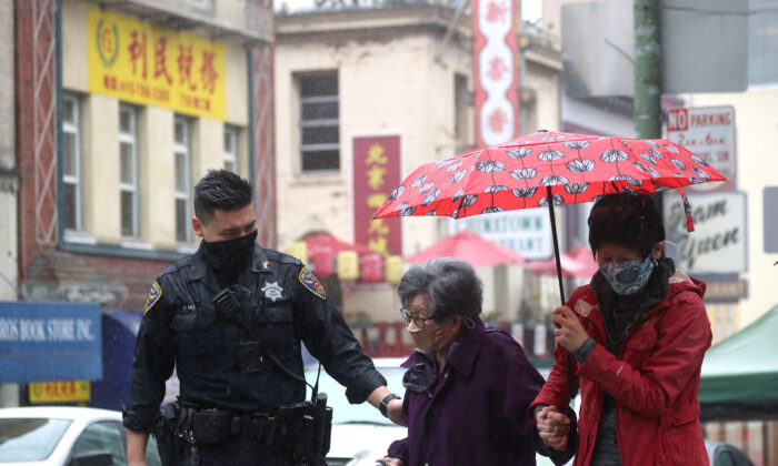 San Francisco police officer William Ma helps an elderly woman cross the street while on a foot patrol in Chinatown on Mar. 18, 2021 in San Francisco, Calif. (Justin Sullivan/Getty Images)