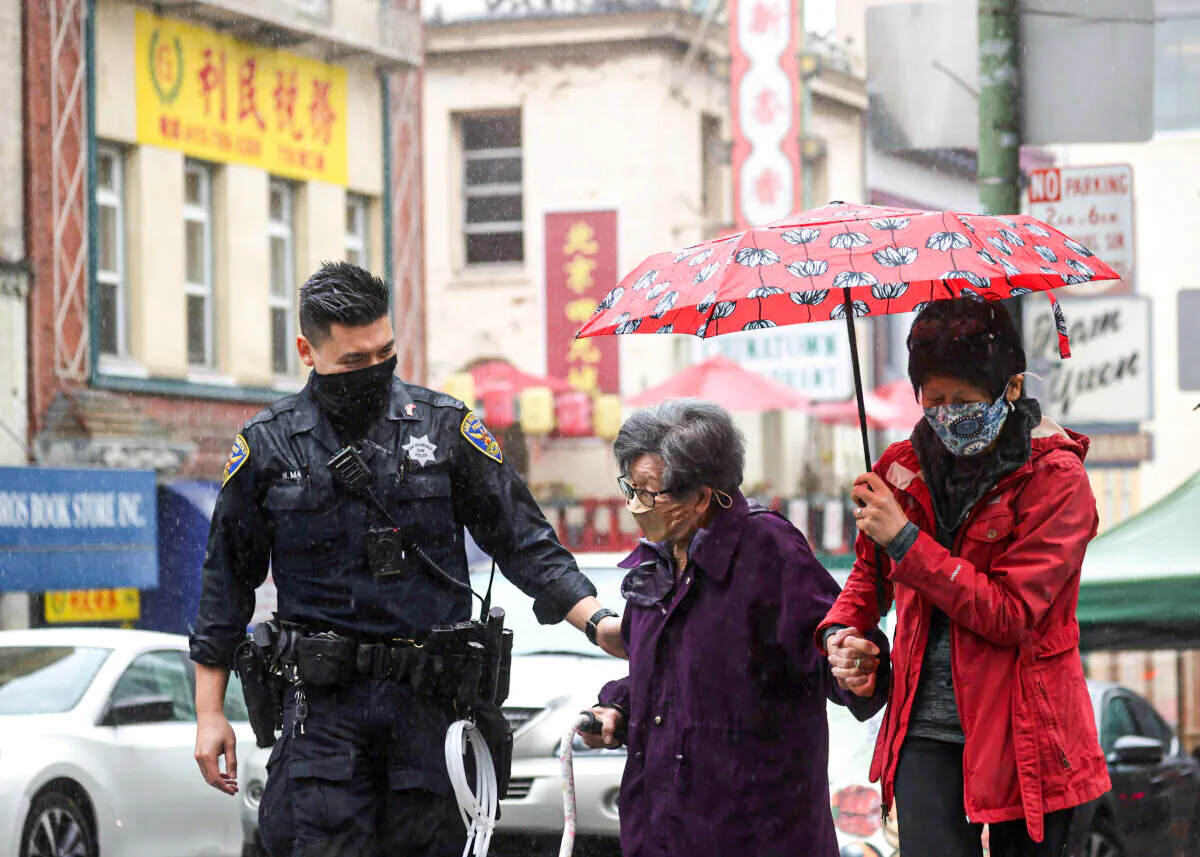 San Francisco police officer William Ma helps an elderly woman cross the street while on a foot patrol in Chinatown on Mar. 18, 2021 in San Francisco, Calif. (Justin Sullivan/Getty Images)