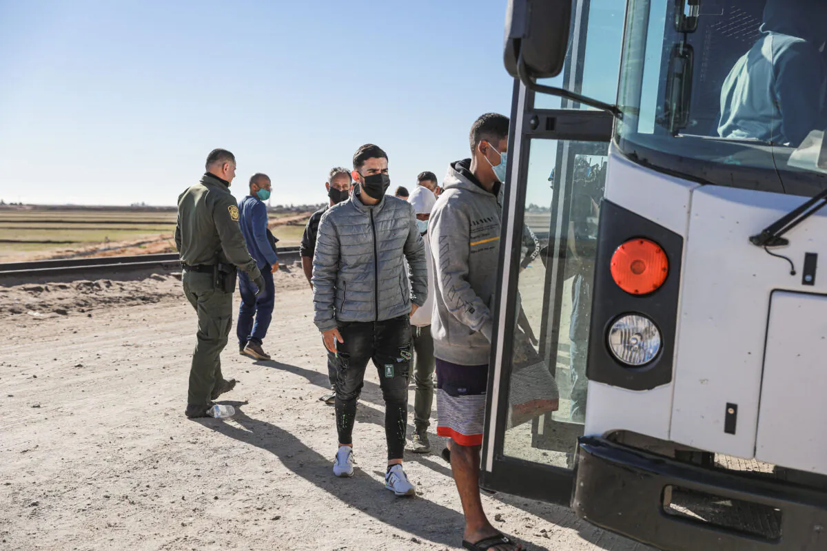 Illegal immigrants who have gathered by the border wall board a bus going to to the Border Patrol station for processing in Yuma, Ariz., on Dec. 10, 2021. (Charlotte Cuthbertson/The Epoch Times)