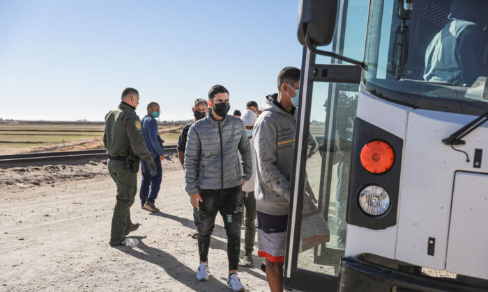 Illegal immigrants who have gathered by the border wall board a bus going to to the Border Patrol station for processing in Yuma, Ariz., on Dec. 10, 2021. (Charlotte Cuthbertson/The Epoch Times)