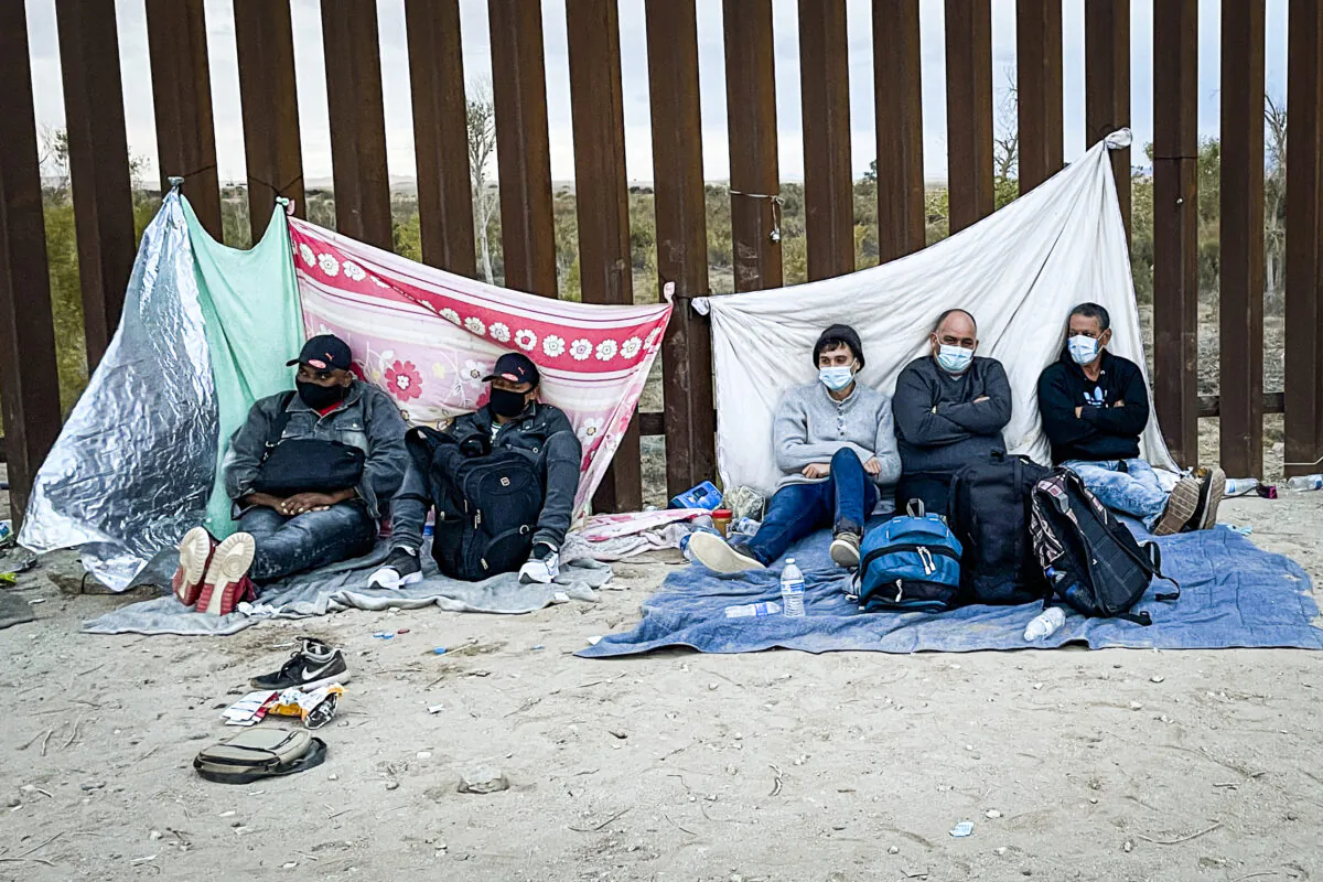 Illegal immigrants wait for Border Patrol by the border fence after crossing the U.S.–Mexico border in Yuma, Arizona, on Dec. 9, 2021. (Charlotte Cuthbertson/The Epoch Times)