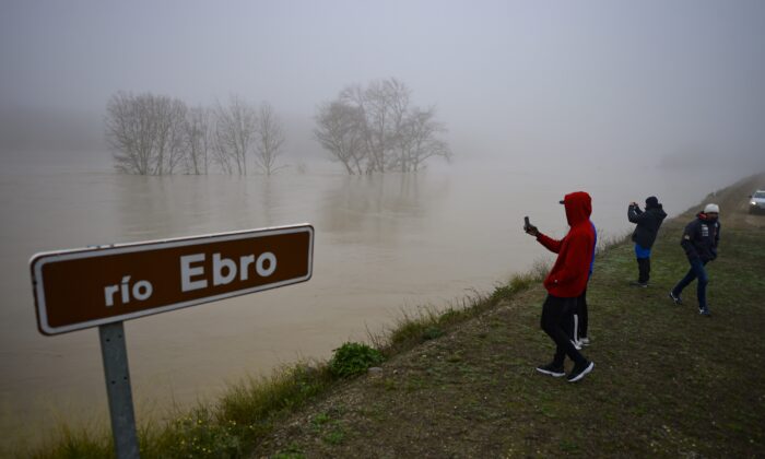 People stand beside the border of flooded area near the Ebro River, in the small village of Pradilla de Ebro, Aragon province, northern Spain, on Dec. 13, 2021. (Alvaro Barrientos/AP Photo)