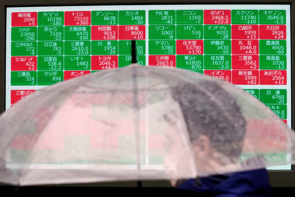 A man wearing a protective mask walks in front of an electronic stock board showing Japan's Nikkei 225 index at a securities firm in Tokyo, Japan, on Dec. 14, 2021. (Eugene Hoshiko/AP Photo)