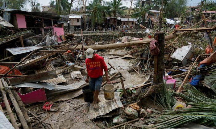 A man carries pails beside damaged homes due to Typhoon Rai in Talisay, Cebu province, central Philippines, on Dec. 17, 2021. (Jay Labra/AP Photo)