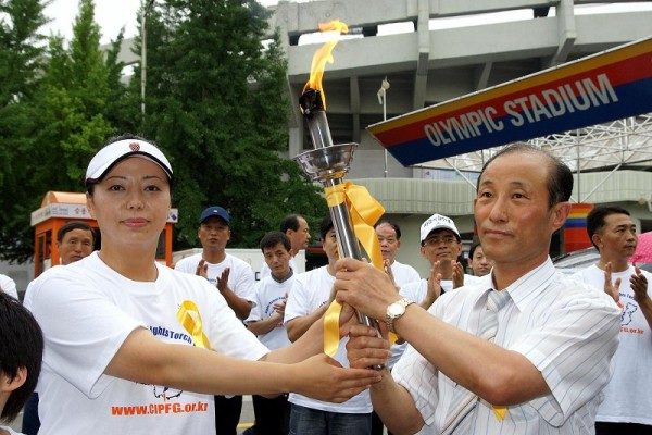 Huang Xiaomin (L), the Human Rights Torch Asian ambassador, hands the torch to Jeong Gujin (R), the vice chair of Asia branch of CIPFG (Coalition to Investigate the Persecution of Falun Gong), at the Olympic Stadium in Seoul, South Korea, on July 2, 2007. (Kim Kukhwan/Epoch Times)