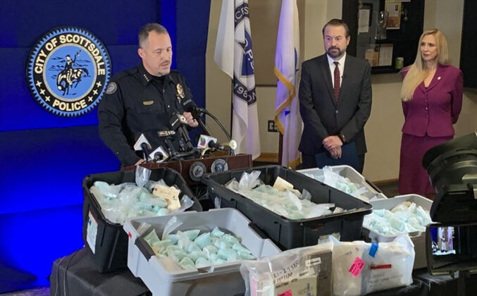 L-R: Scottsdale Police Chief Jeff Walther in front of a display of illicit fentanyl-laced pills and other narcotics; Arizona Attorney General Mark Brnovich, and Cheri Oz, special agent in charge of the DEA’s Phoenix field division at a press conference in Scottsdale, Ariz., on Dec. 16, 2021. (Scottsdale PD)