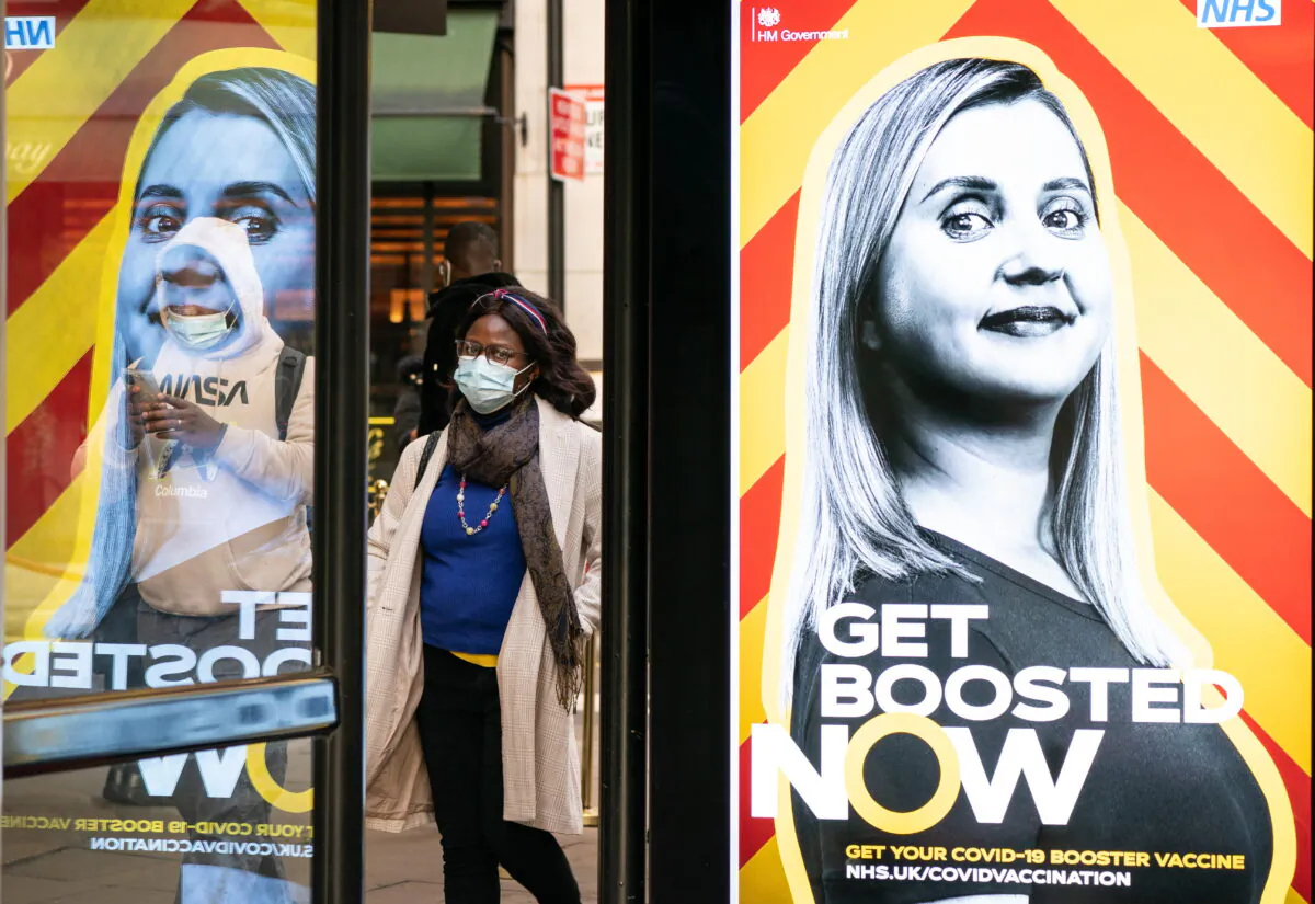 People wearing masks walk past a UK government advert encouraging people to book a COVID-19 booster vaccine, in an undated file photo. (Dominic Lipinski/PA)