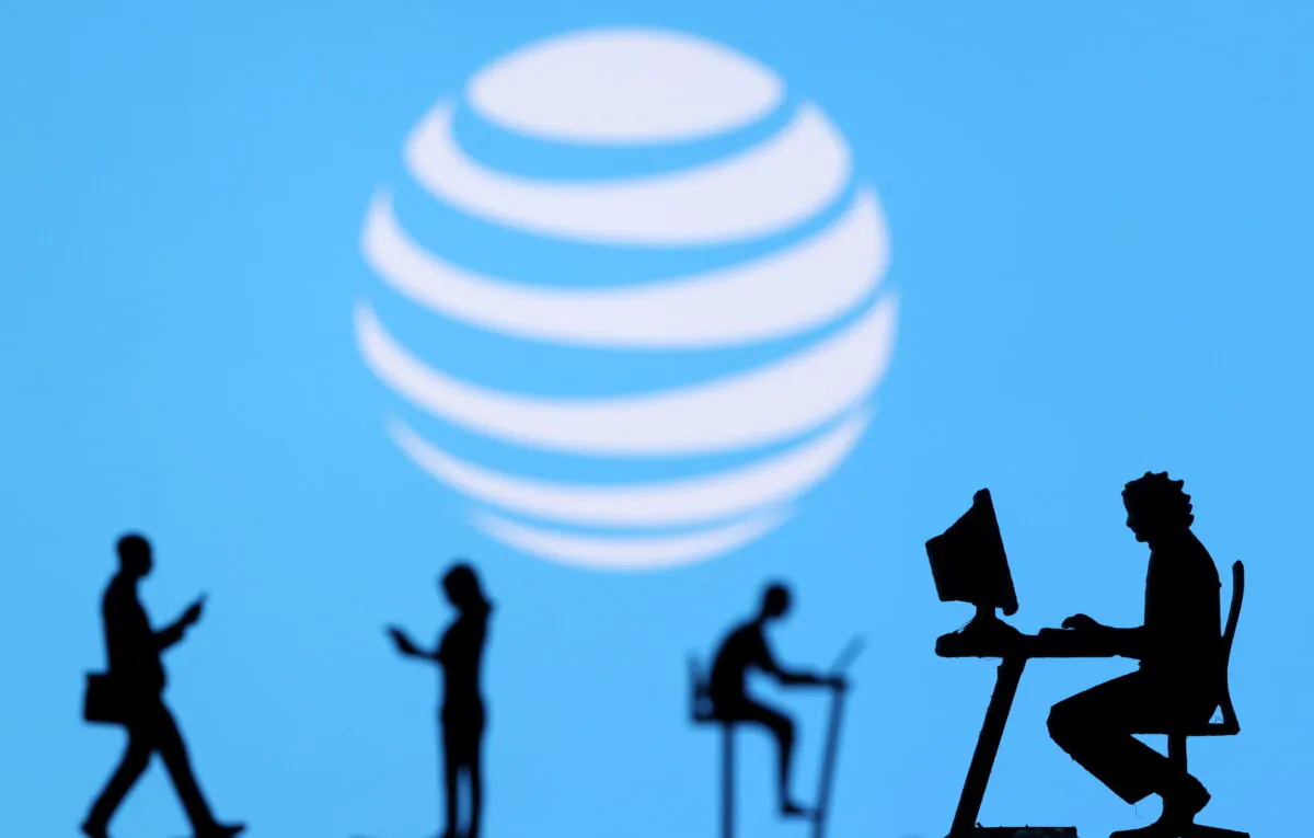 Small toy figures with laptops and smartphones are seen in front of  a displayed AT&T logo, in this illustration taken on Dec. 5, 2021. (Dado Ruvic/Illustration/Reuters)